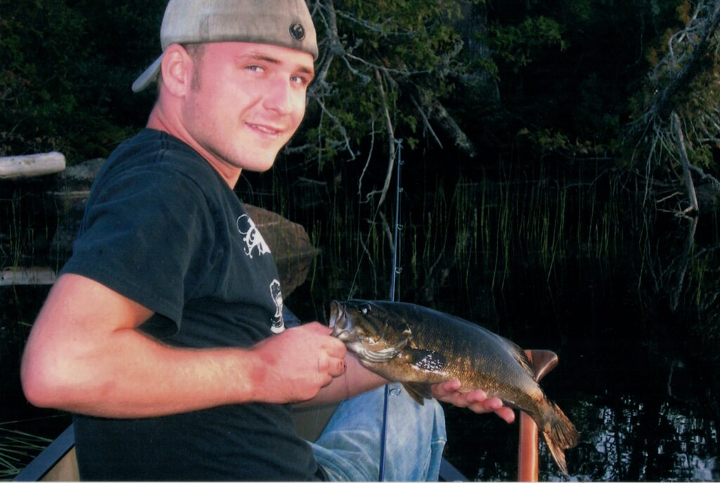A man in a backwards baseball cap holds up a fish.