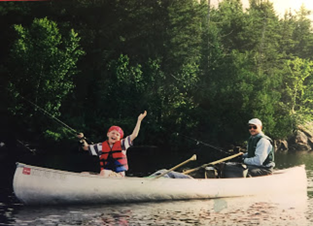 A boy throws up his arms in the front of an aluminum canoe