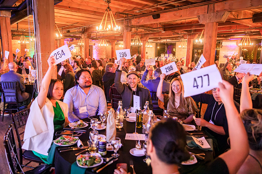 A tableful of smiling BWCA gala attendees hold up auction bidding numbers