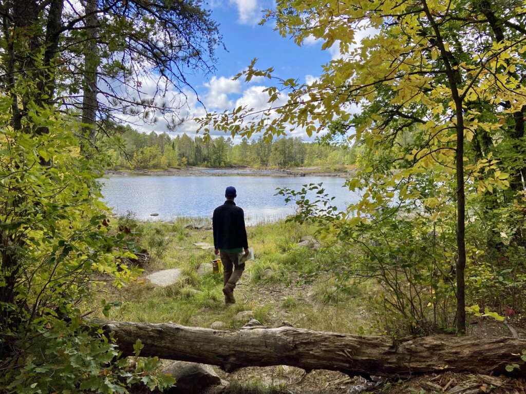 A slender man gazes out towards a BWCA lake as he walks towards it. Photo by Amy Marty.