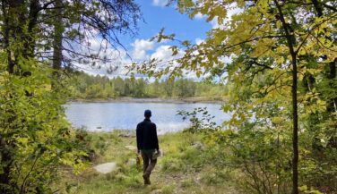 A slender man gazes out towards a BWCA lake as he walks towards it. Photo by Amy Marty.