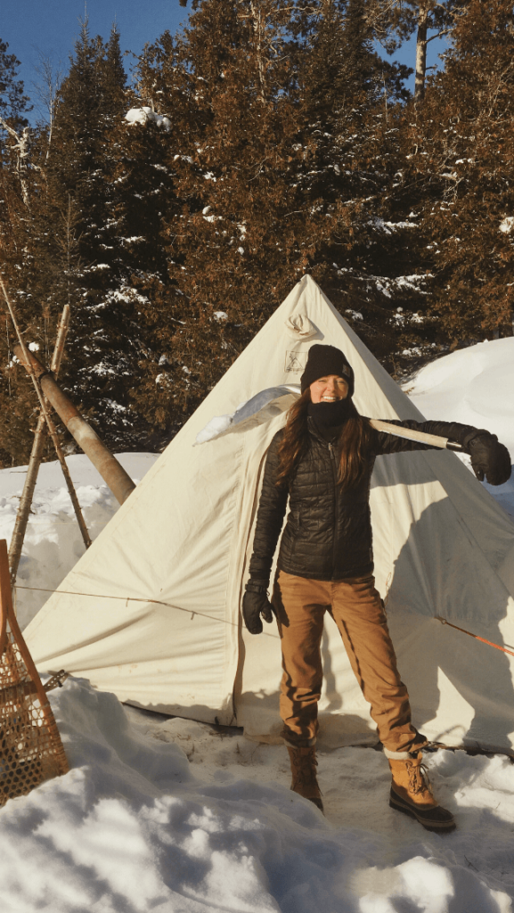Stay warm in a hot tent in winter in the BWCA Ashley Bredemus in down coat and hot tent winter camping Boundary Waters