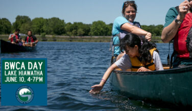 Girl reaching down from a canoe in a lake to touch the water. Text: BWCA Day Lake Hiawatha, June 10, 4-7pm