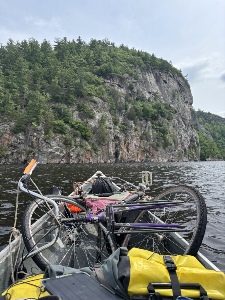 A canoe on the water with a towering rock wall on the horizon and bike loaded in the bow.