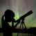 A child and telescope, silhouetted in front of the Northern Lights in the Boundary Waters.
