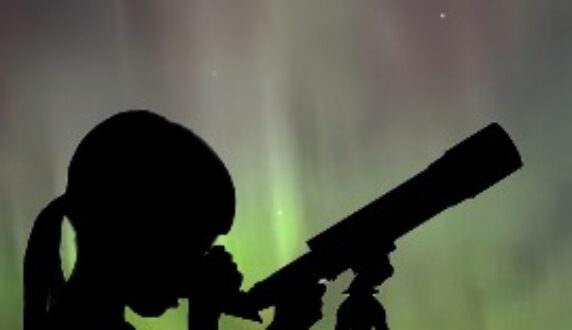 A child and telescope, silhouetted in front of the Northern Lights in the Boundary Waters.