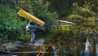 Aman at waters edges takes a canoe down from his shoulders