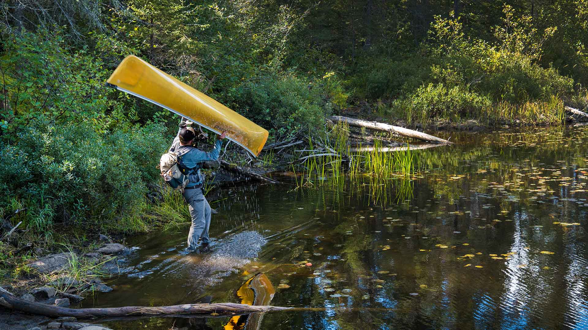A man at waters edges takes a canoe down from his shoulders
