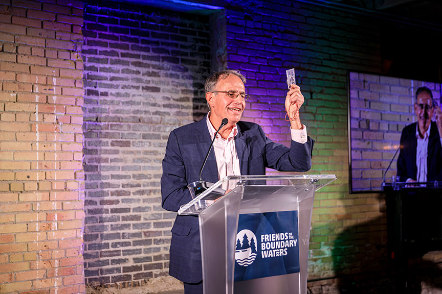 A smiling Chris Knopf holds up a compass at a podium.