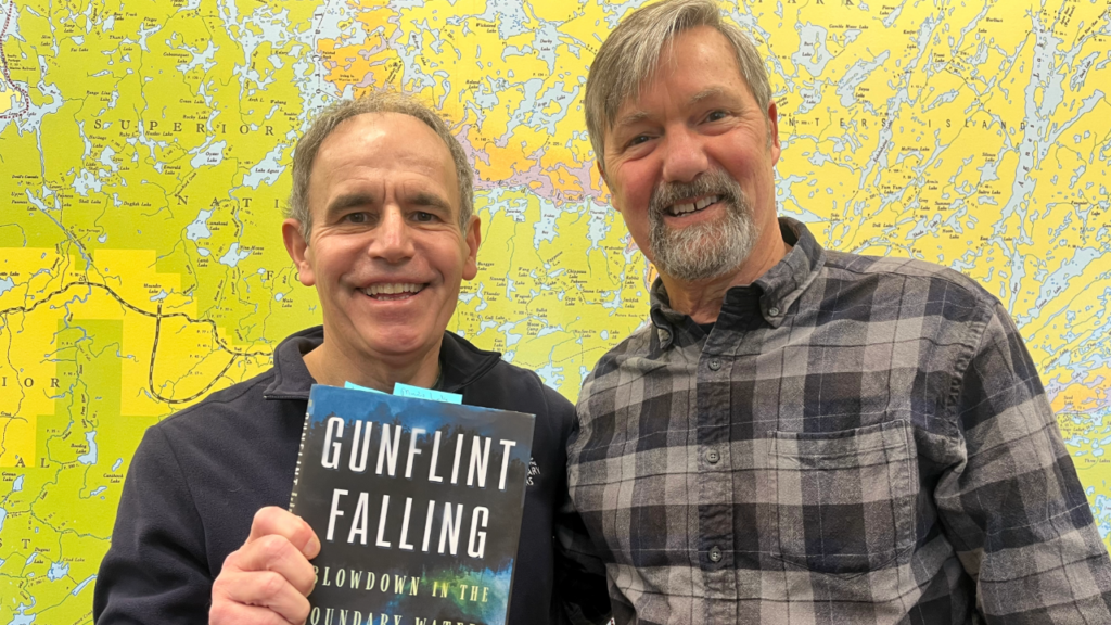 Chris Knopf standing in front of a BWCA map with Cary Griffith, holding up his book Gunflint Falling