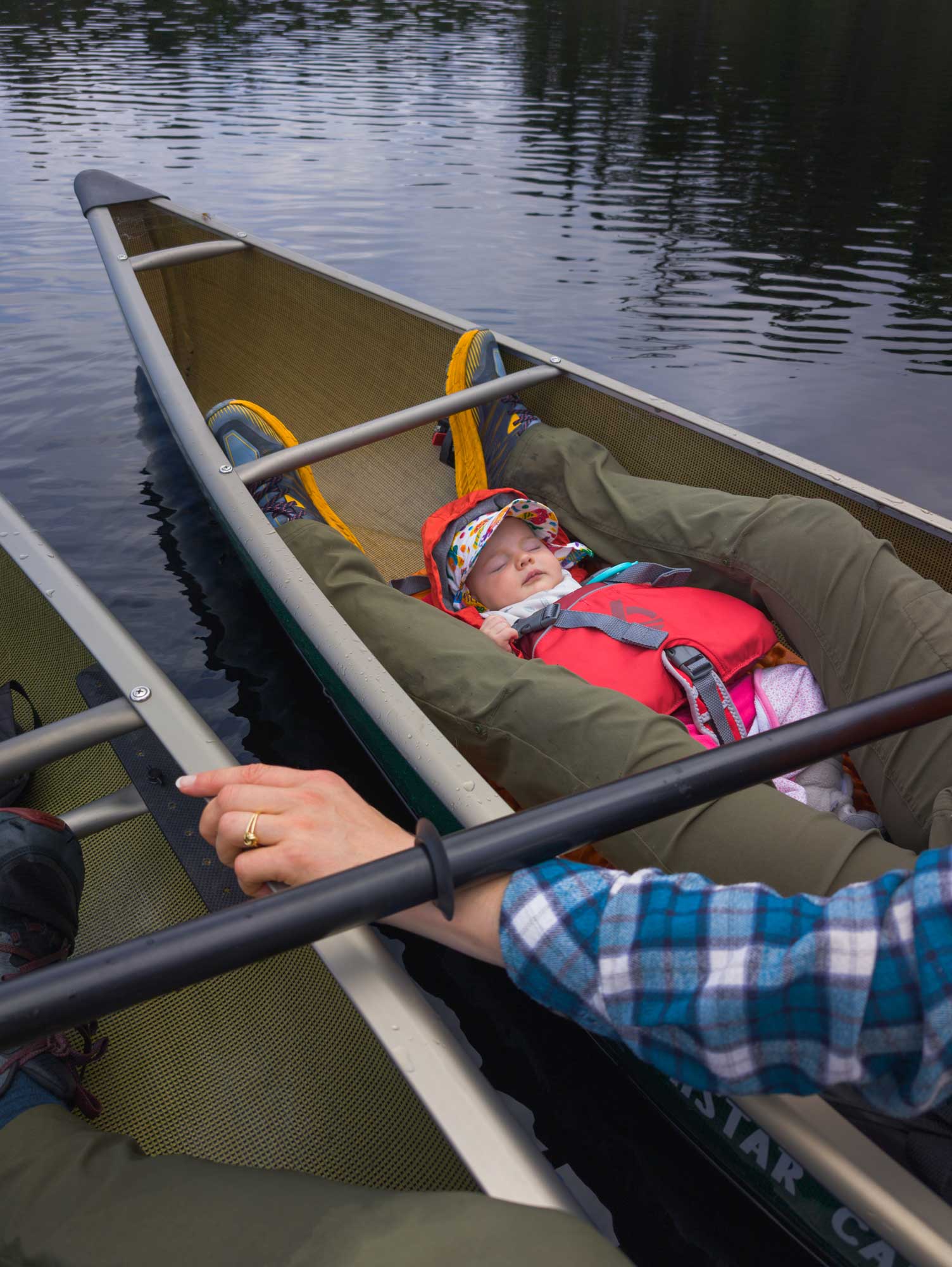 A baby sleeps soundly, bundled up in a canoe on a lake in the Boundary Waters.