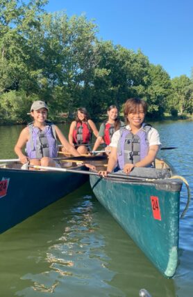 Four students smiling, in two green canoes pulled side by side in a lake
