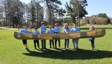 A group of students lifting a canoe in a field in Minnesota