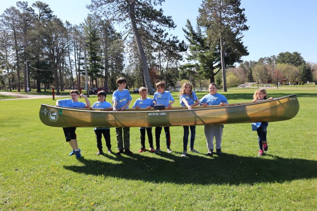 A group of students lifting a canoe in a field in Minnesota