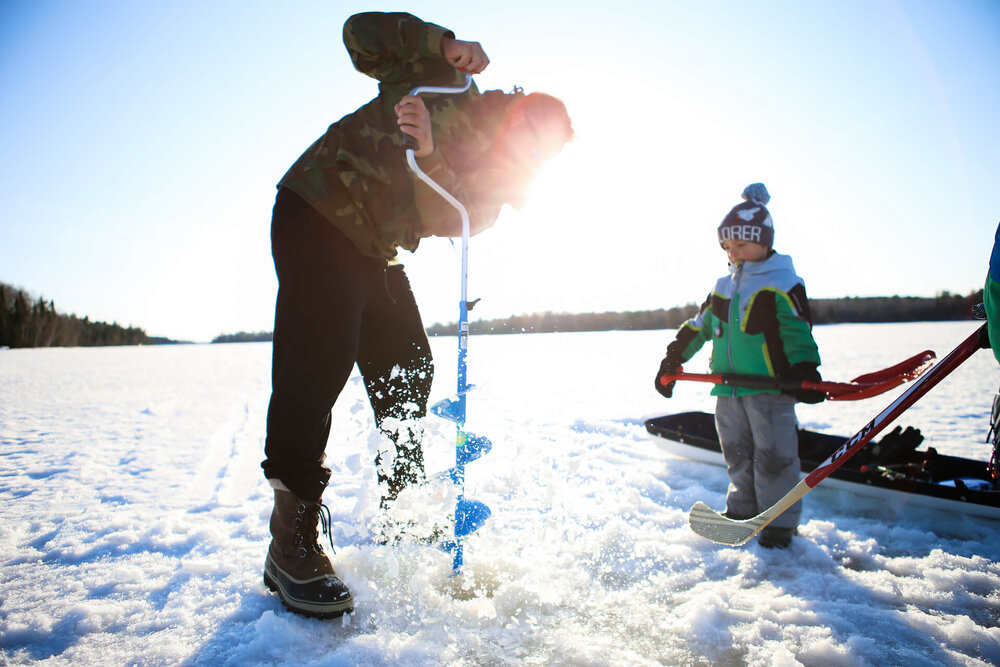 A parent and child drilling on a frozen lake with an ice auger in the BWCAW