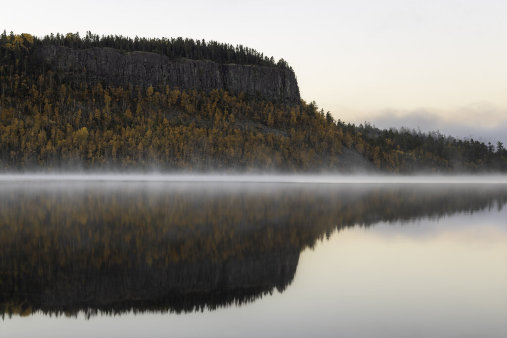 Clearwater Lake palisade, with golden trees is reflected in misty waters.