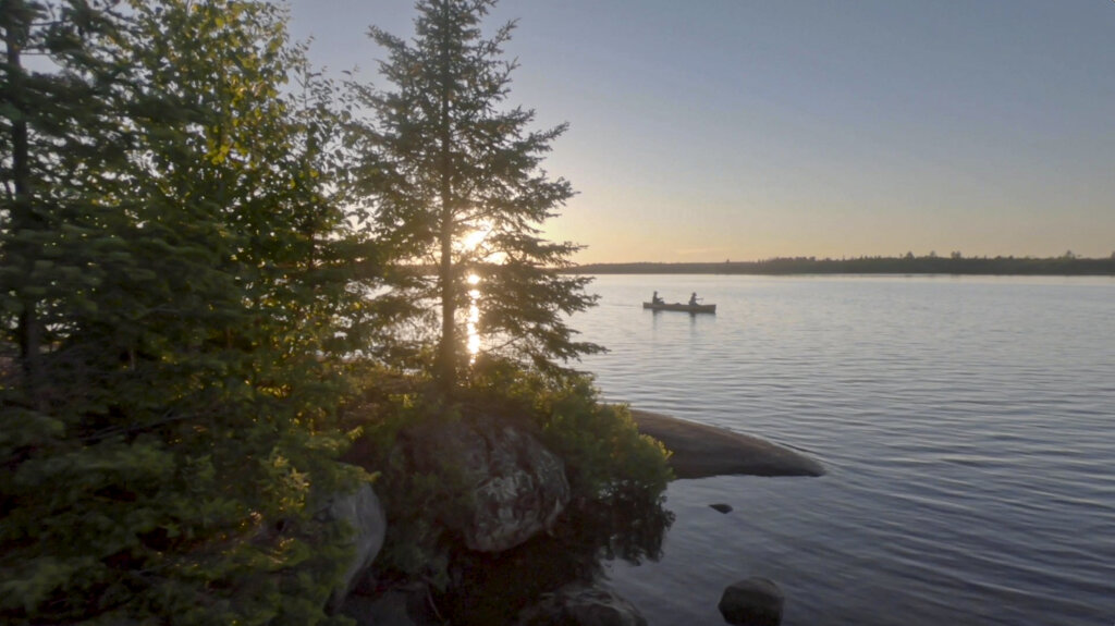Photo: Josh Meltzer A canoe comes around the corner in the Boundary Waters, framed by a fading sun through the trees on the horizon.