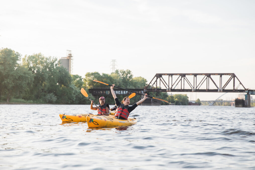 A young woman and man paddling yellow kayaks on the Mississippi River with a bridge in the background.
Photo courtesy of Mississippi Park Connection