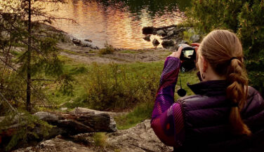A woman pointing a camera, taking a photo of a BWCA sunset