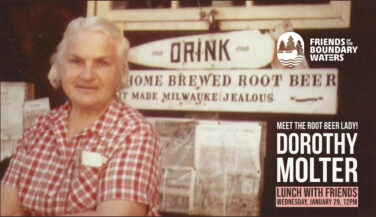 Dorothy Molter standing in front of a building advertising her root beer.