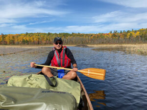 A man in a red life jacket in a canoe in the Boundary Waters - paddle poised to dip in the water.