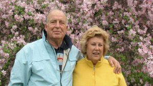 An older couple, standing in front of lilacs