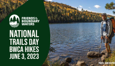 Photo: John Keefover A bearded man with hiking poles stands next to a lake in the BWCA. Text: Friends of the Boundary Waters National Trails Day BWCA Hikes June 3, 2023