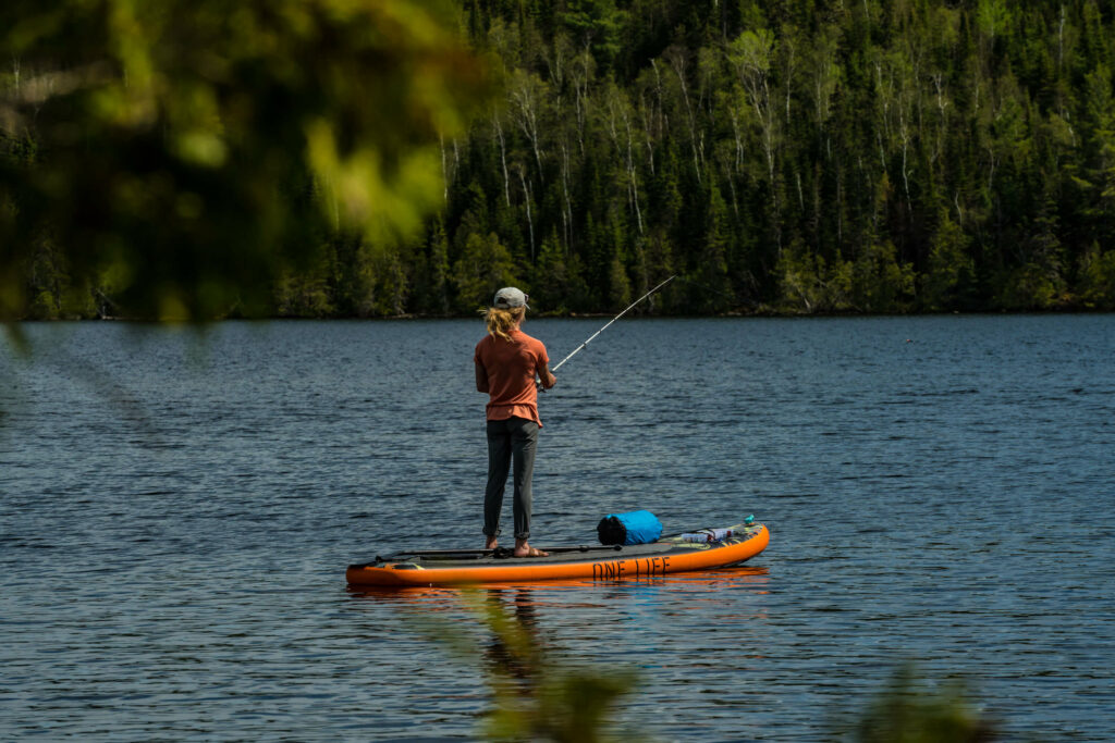 A woman fishing while standing on her stand up paddle board.