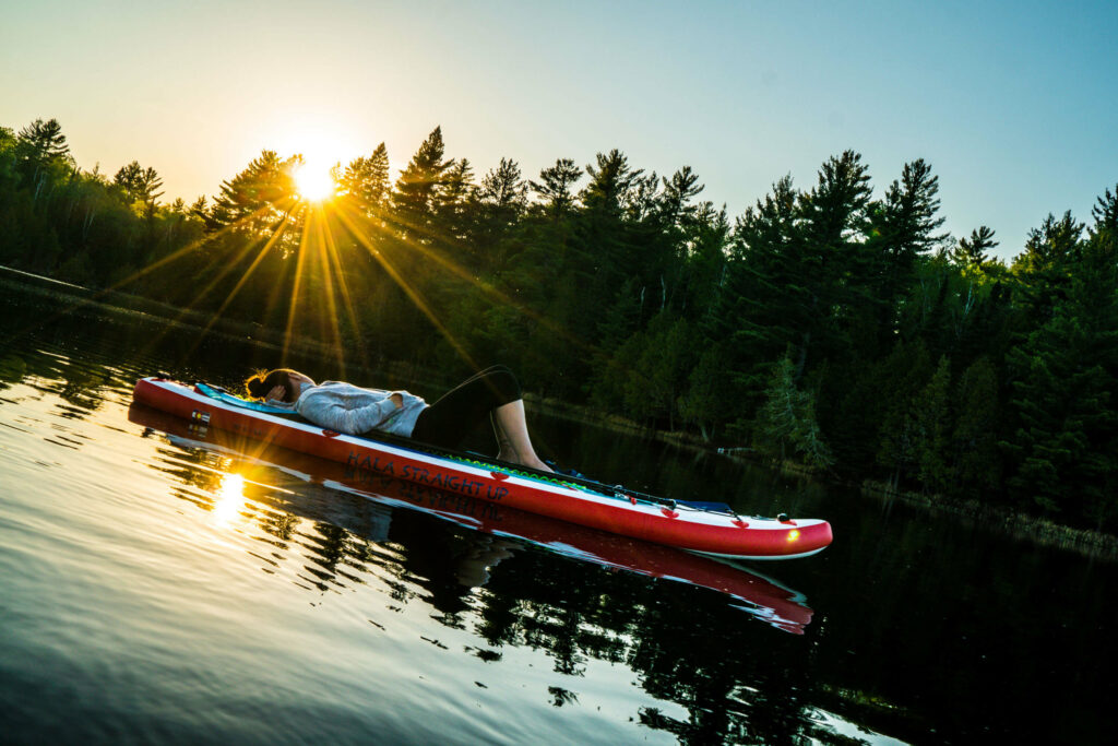 Image of a woman watching the sunset while laying on her paddle board.