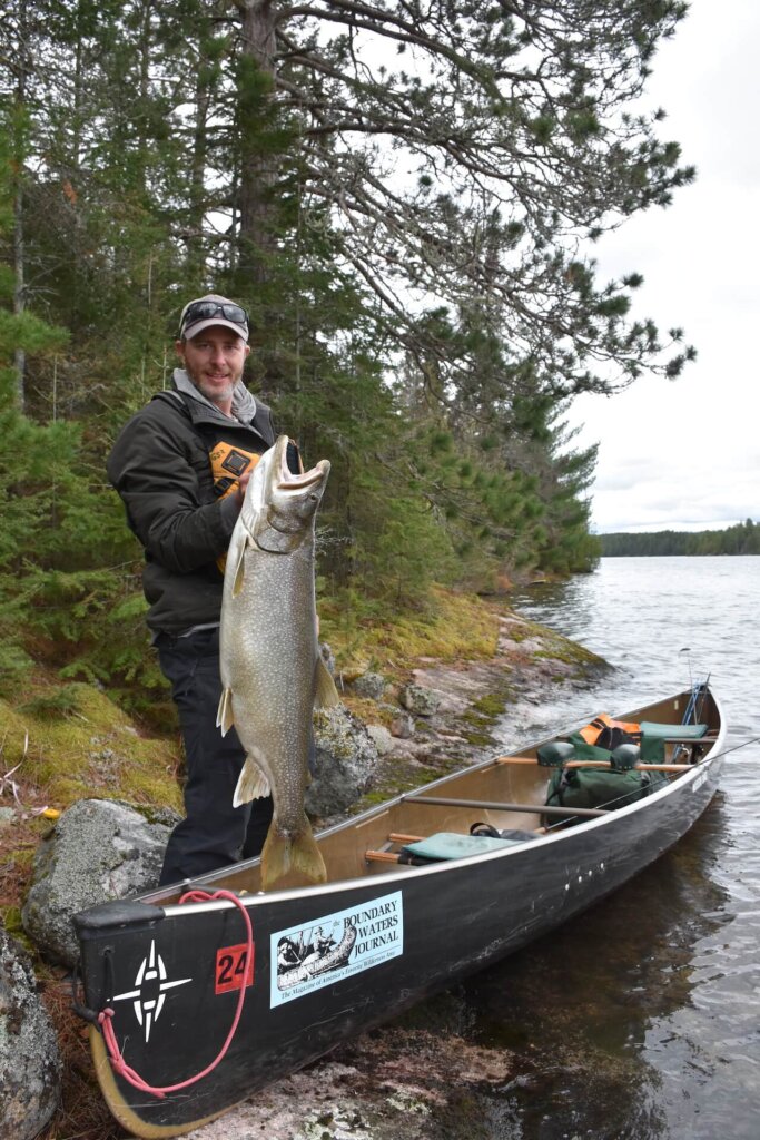 Man holding a giant Lake Trout next to a canoe in the Boundary Waters