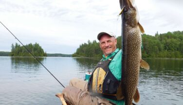 A man in a canoe holds up a giant Northern Pike in the Boundary Waters.