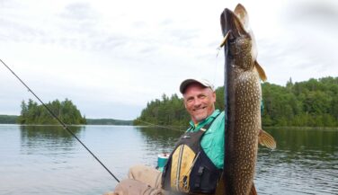 A man in a canoe holds up a giant Northern Pike in the Boundary Waters.