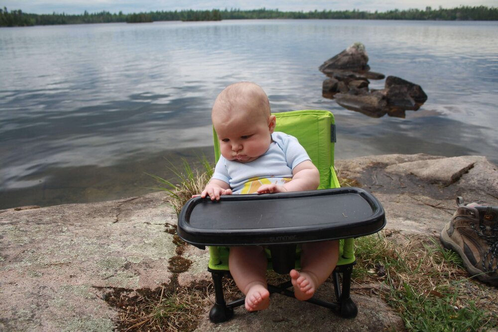 Drooling baby sitting on a chair by the lake in the BWCA