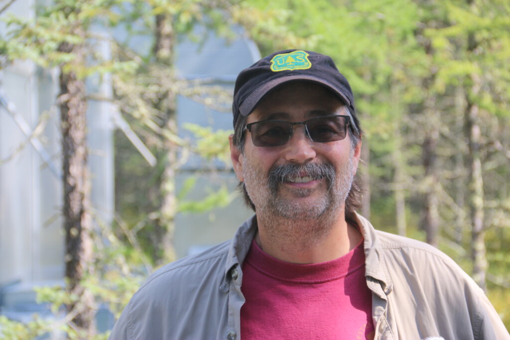 A mustachioed gentleman in shaded glasses and a U.S. Forest Service ballcap.