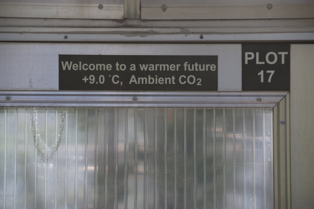 A sign reading "Welcome to a warmer future +9.0 degrees C, Ambient CO2 Plot 17"