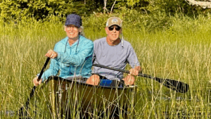A woman and a man paddle in the high grass