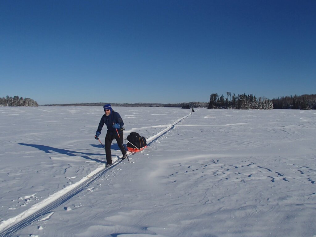 skier pulling a sled while winter camping Cross country skiing in Boundary Waters, Minnesota with a ski pulk or sled
