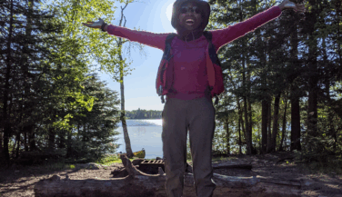 Bionca Davis arriving at a BWCA campsite, with arms outstretched, in the sun.