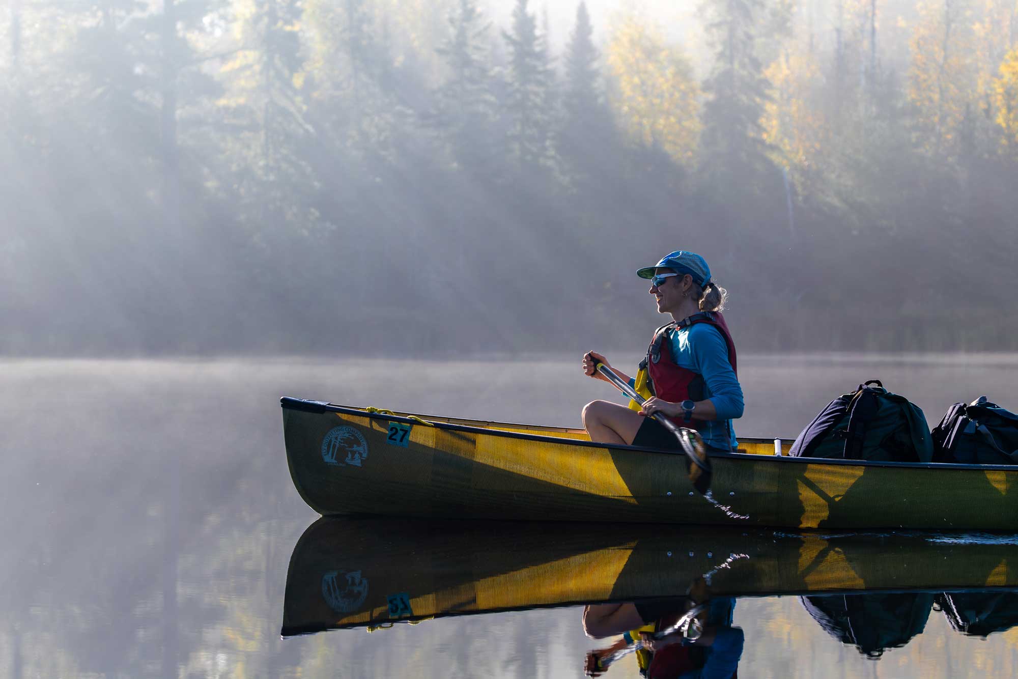A woman smiling as she paddles along a clear and still boundary waters lake.