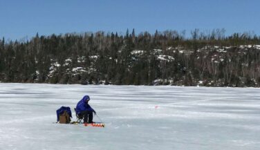 Man ice fishing in the middle of an icy lake.