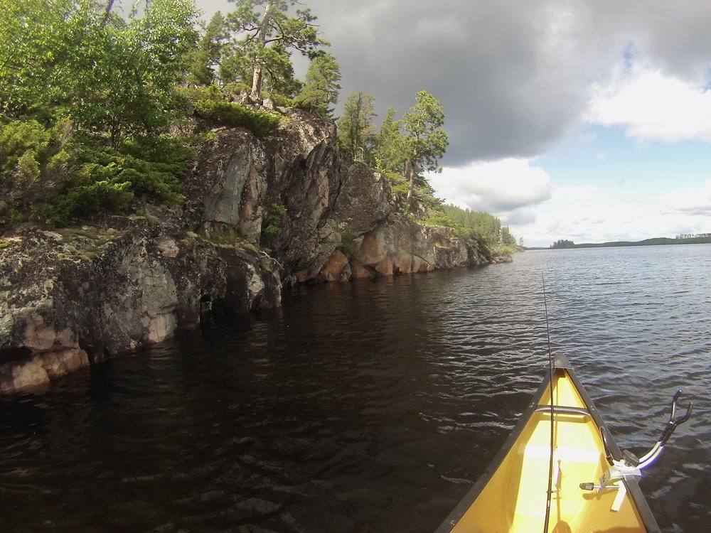 Canoe with fishing pole next to a steep rock face